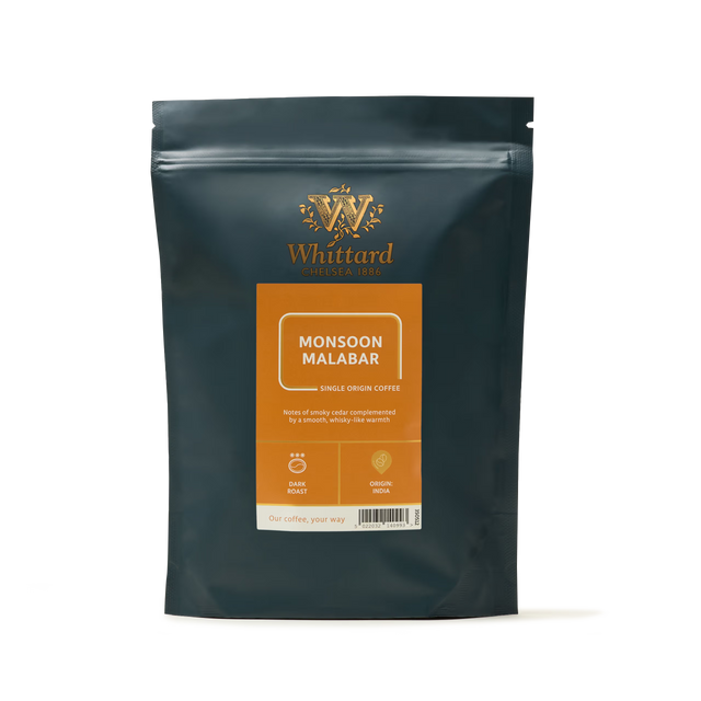 A dark green coffee bag labeled Monsoon Malabar Coffee, adorned with orange and gold accents, stands upright against a white background. This eye-catching package emphasizes the rich heritage of Indian coffee and suggests the bold flavor characteristic of this dark roast.