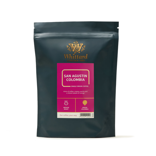 A black coffee bag labeled San Agustin Colombia Coffee with gold and pink accents showcases icons for medium roast and origin, alongside descriptive text highlighting the creamy texture and orange flavor notes of Colombian Arabica—ideal for those seeking a specialty coffee experience.