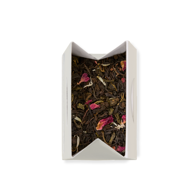 Afternoon Tea Loose Leaf Tea blend with rose petals and green leaves inside an open white paper tea sachet, viewed from above on a white background—perfect for elevating your afternoon tea with its fragrant oolong and jasmine green tea notes.
