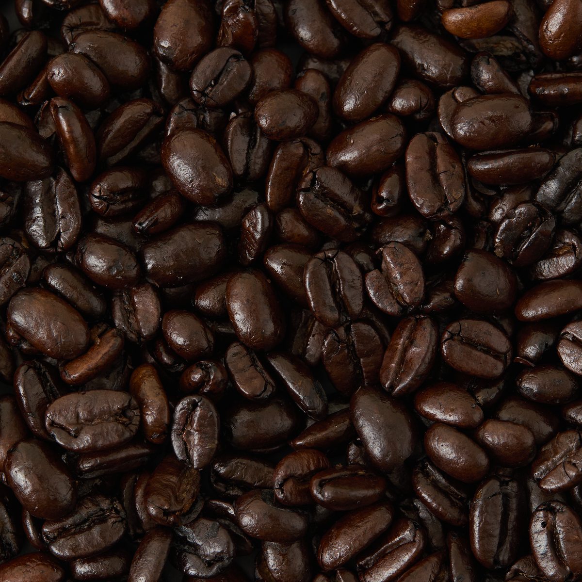 A close-up view of Old Brown Java Coffee beans, highlighting their glossy, dark brown surfaces and rich texture reminiscent of bold peppercorn spice.
