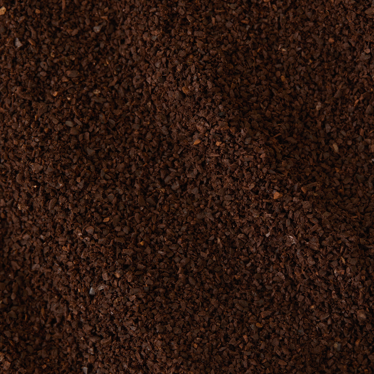 A close-up view of dark brown Old Brown Java Coffee grounds reveals a coarse texture and uneven surface, hinting at the robust character and subtle bold peppercorn spice notes unique to this aged coffee.