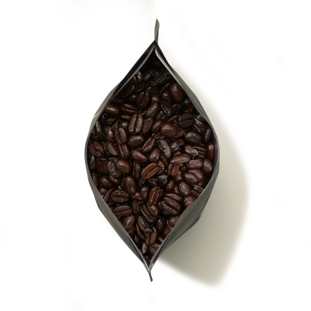 A top view of an open black bag of Old Brown Java Coffee filled with dark roasted coffee beans, set against a plain white background.