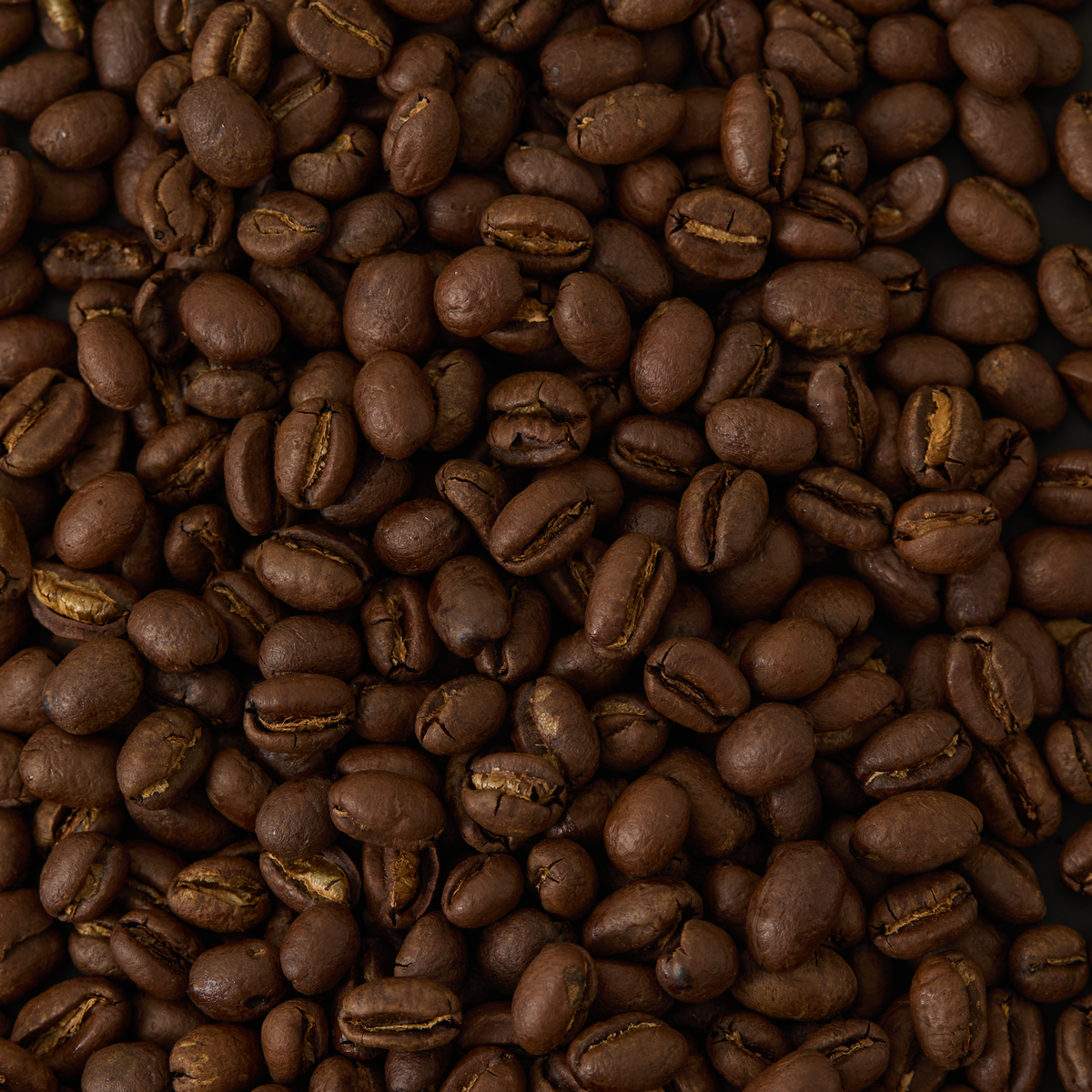 A close-up view of a large pile of Kenya Peaberry Coffee beans, highlighting their rich brown color and glossy texture.