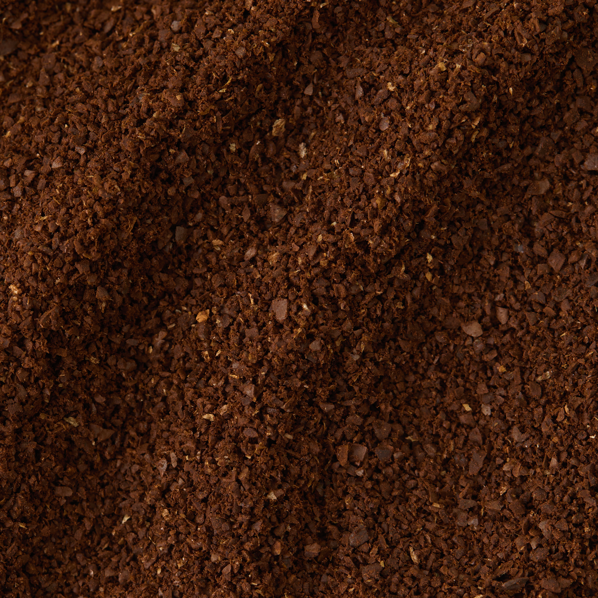 Close-up of a pile of ground Kenya Peaberry Coffee, showing a textured, dark brown surface with small, uneven granules.