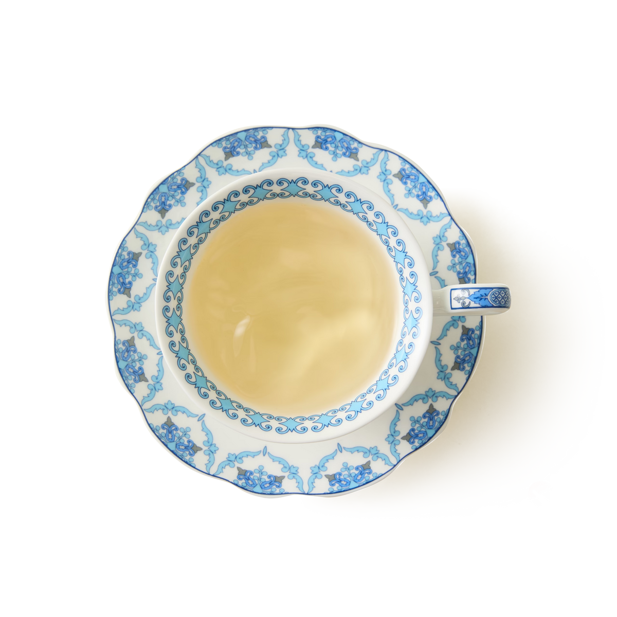 A top view of a cup of tea in a porcelain teacup with a blue floral pattern on a white background.
