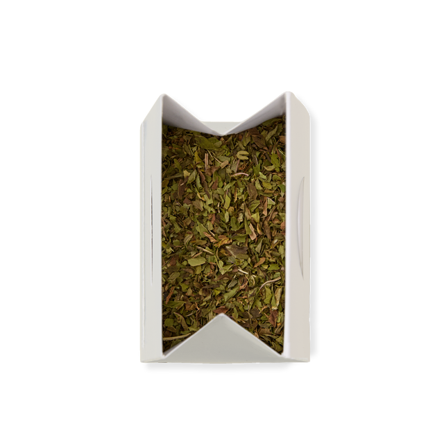 A white, rectangular container filled with Peppermint Loose Infusion—dried, chopped green herbs—is viewed from above against a plain white background.