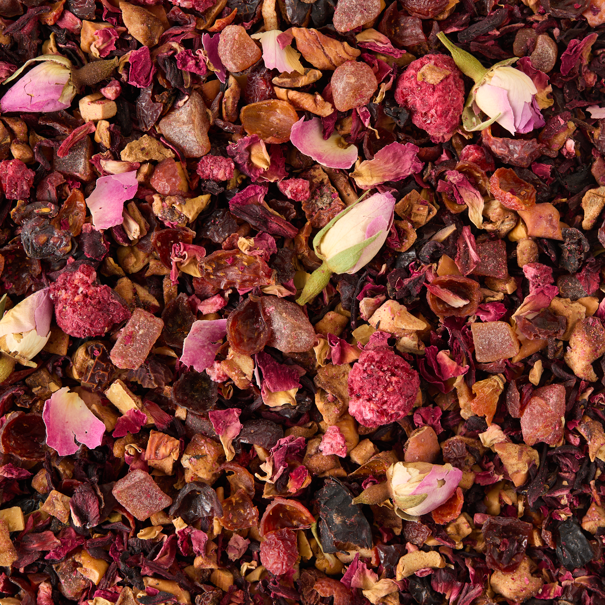 A close-up of Peach, Raspberry & Rose Loose Infusion, showcasing a blend of dried fruit pieces, rose petals, whole rosebuds, and assorted herbs in vibrant shades of pink, red, and brown.