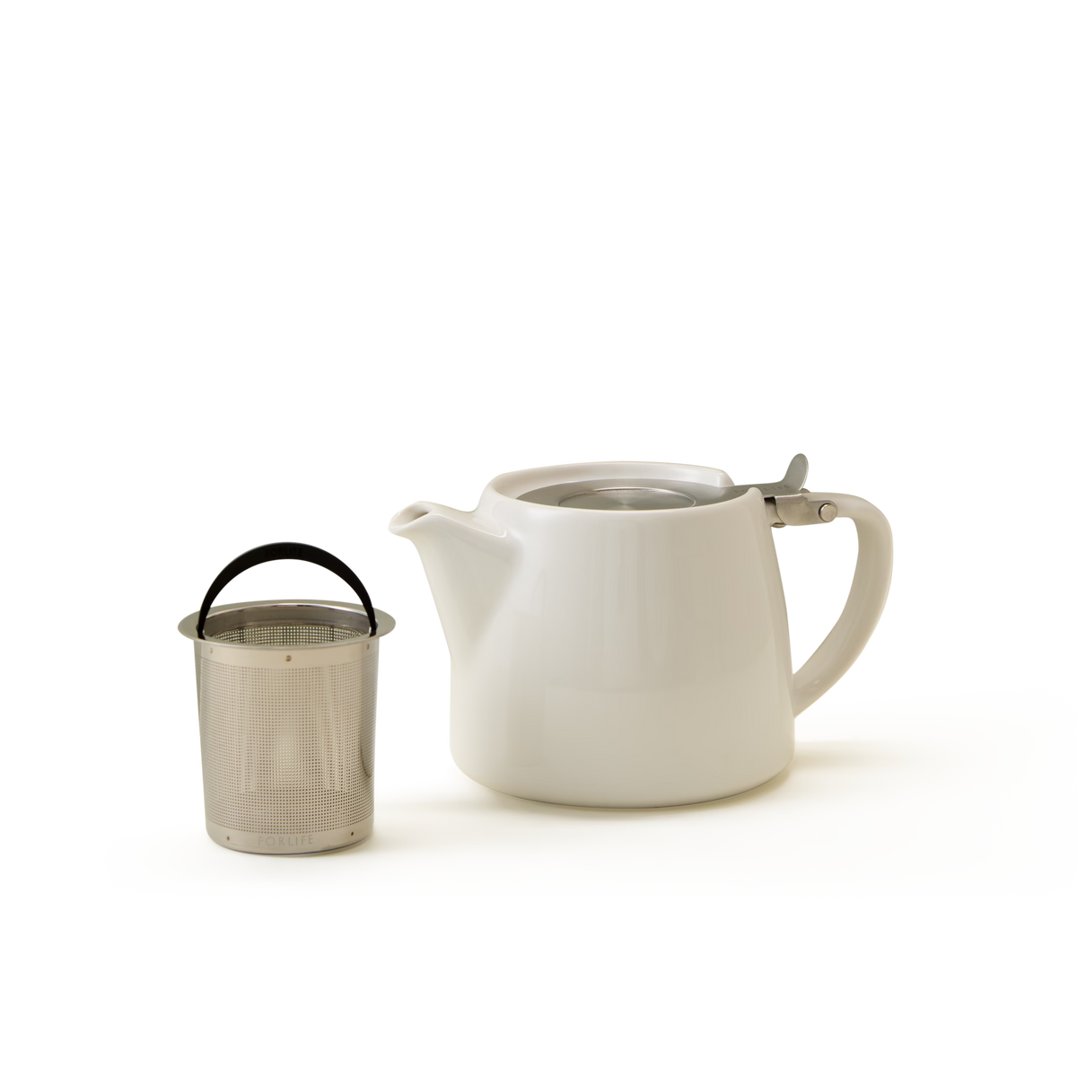 A white ceramic teapot with a handle and spout is placed next to a metal tea infuser with a black handle, set against a plain white background.