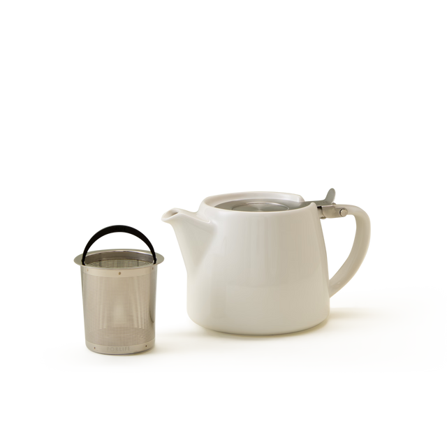 A white ceramic teapot with a handle and spout is placed next to a metal tea infuser with a black handle, set against a plain white background.