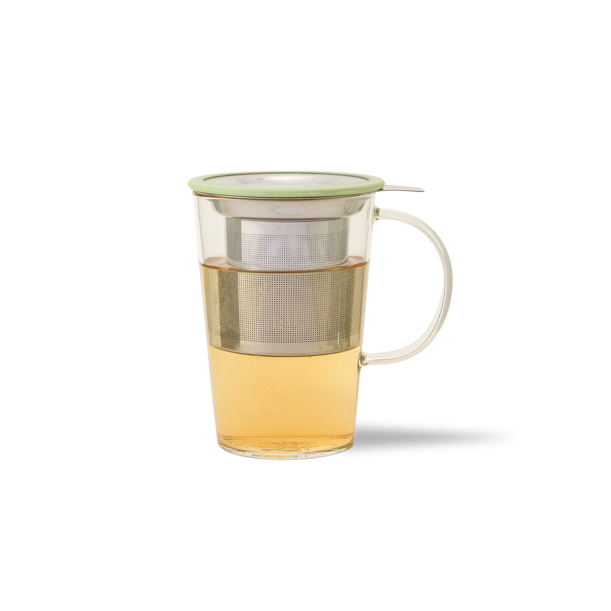 A glass mug with a handle, filled with light amber tea. A metal tea infuser is inside the mug, and a light green lid rests on top. The background is plain white.