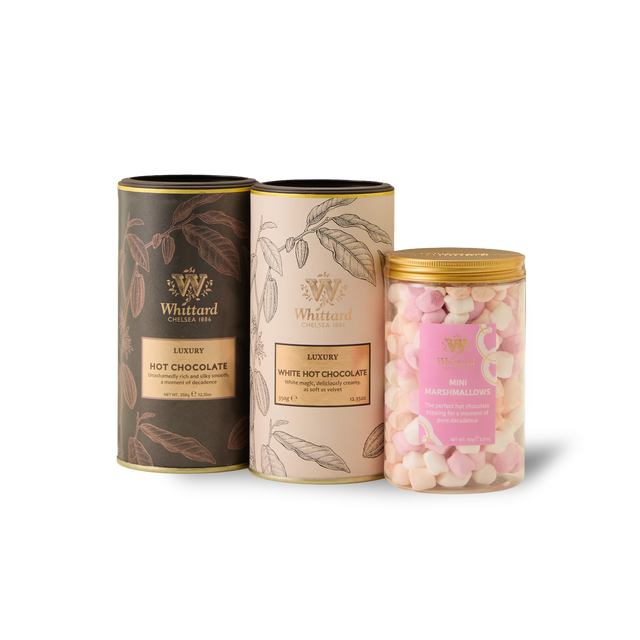 Three Whittard containers from The Luxury Hot Chocolate Gift Box—one black tin for luxury hot chocolate, one cream tin for white hot chocolate, and a clear jar filled with pink and white mini marshmallows—are arranged side by side on a white background, creating the perfect hot chocolate gift.