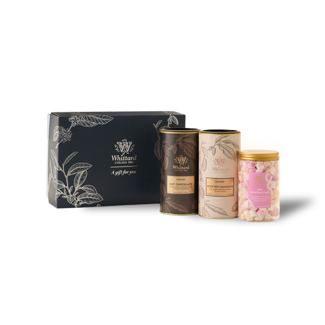 The Luxury Hot Chocolate Gift Box features a dark box containing two tins labeled Hot Chocolate and Luxury White Hot Chocolate, along with a jar filled with pink and white mini marshmallows. All items are neatly arranged on a white background.