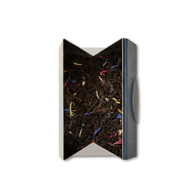 A top view of an opened box containing Regal Blend Loose Leaf Tea, showcasing black tea mixed with colorful flower petals—pink, yellow, and blue—against a white background. This blend nods to British tea traditions and features a delicate infusion of Madagascan vanilla for a fragrant twist.