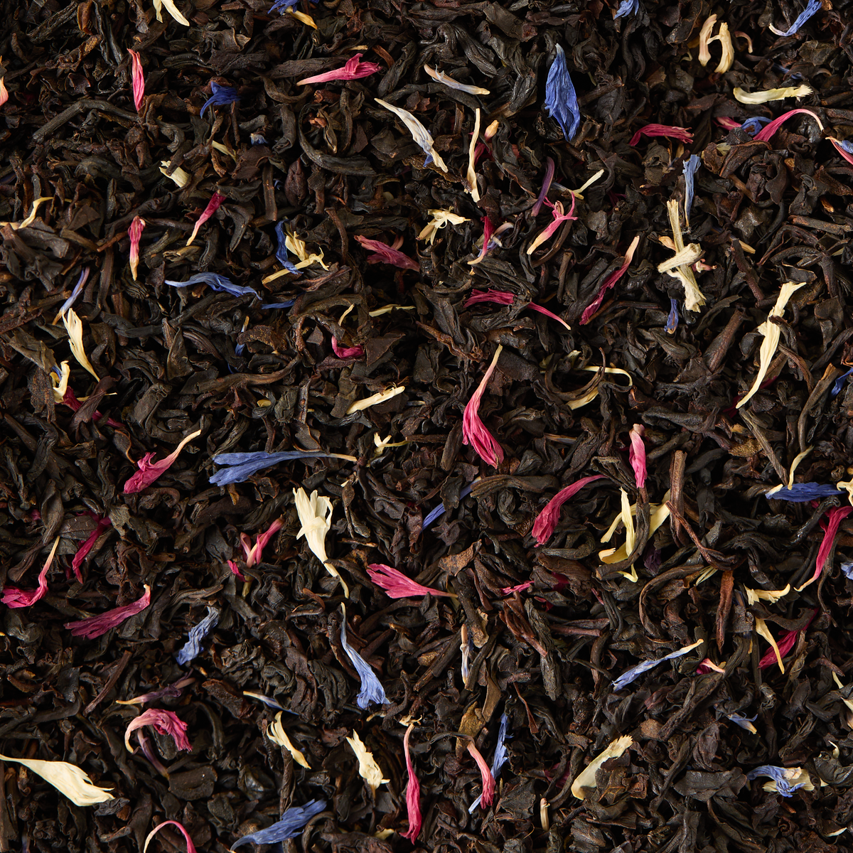 Regal Blend Loose Leaf Tea is a black tea combined with Madagascan vanilla and dried flower petals in pink, blue, and white hues, resulting in a vibrant and textured mixture.