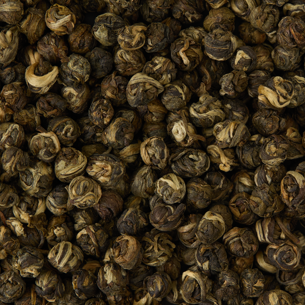 A close-up view of numerous tightly packed, rolled green tea pearls reveals twisted, dry leaves in hues of green and brown—these exquisite Jasmine Dragon Pearls Loose Leaf Tea are a premium selection, expertly handcrafted in China’s Fujian Province.