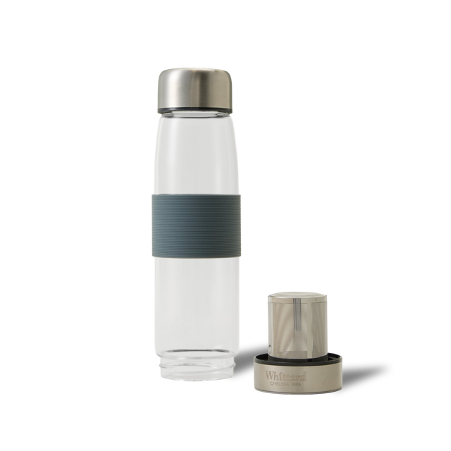 A clear glass water bottle with a grey grip band and silver cap stands upright next to a detached infuser with a matching silver top, both on a plain white background.