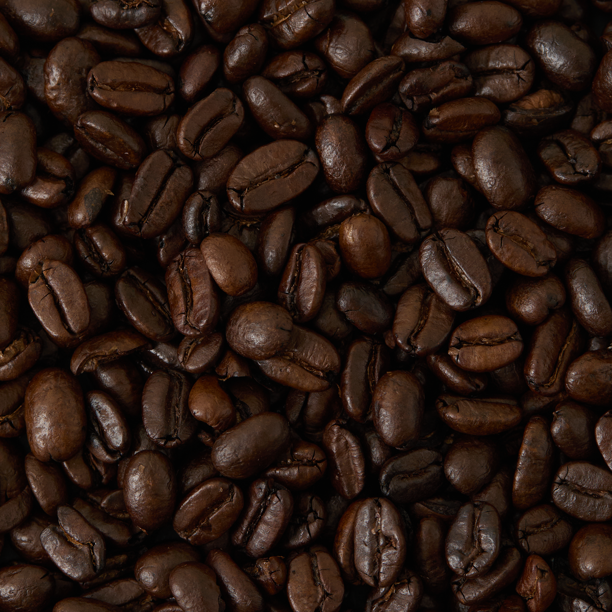 Close-up of a pile of Sumatra Mandheling Coffee beans, dark roasted and processed with the wet-hulling method, highlighting their shiny, textured surfaces and deep brown color that reflects their famously low acidity.