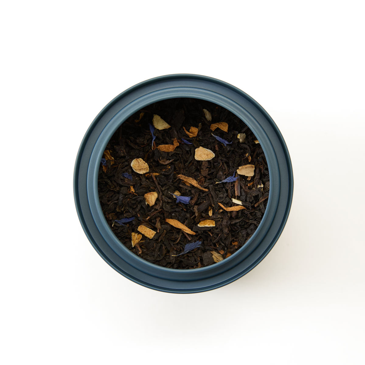 A top-down view of a blue container filled with loose leaf tea, showing dark tea leaves mixed with dried flower petals and small pieces of dried fruit or spices, all on a white background.