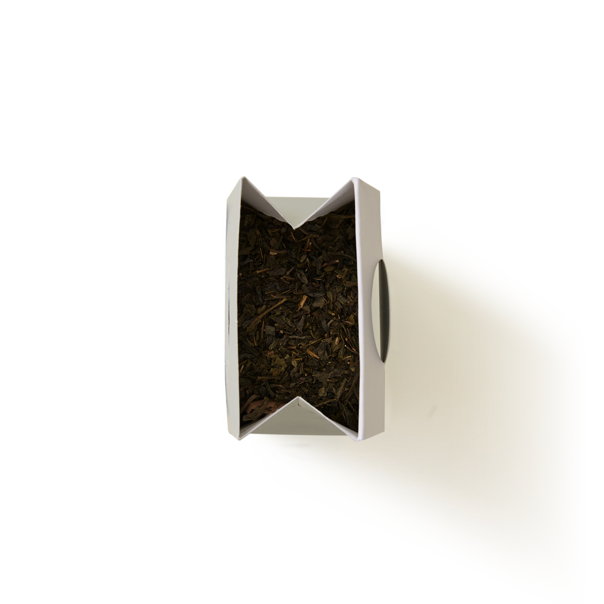 A top-down view of an open white container filled with Classic Green Tea loose leaves against a white background.