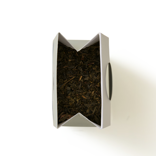 An open cardboard box filled with Classic Green Tea loose-leaf leaves.