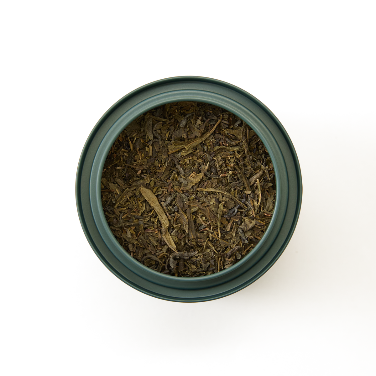 A top view of a dark green container filled with Classic Green Tea loose leaves, set against a plain white background.
