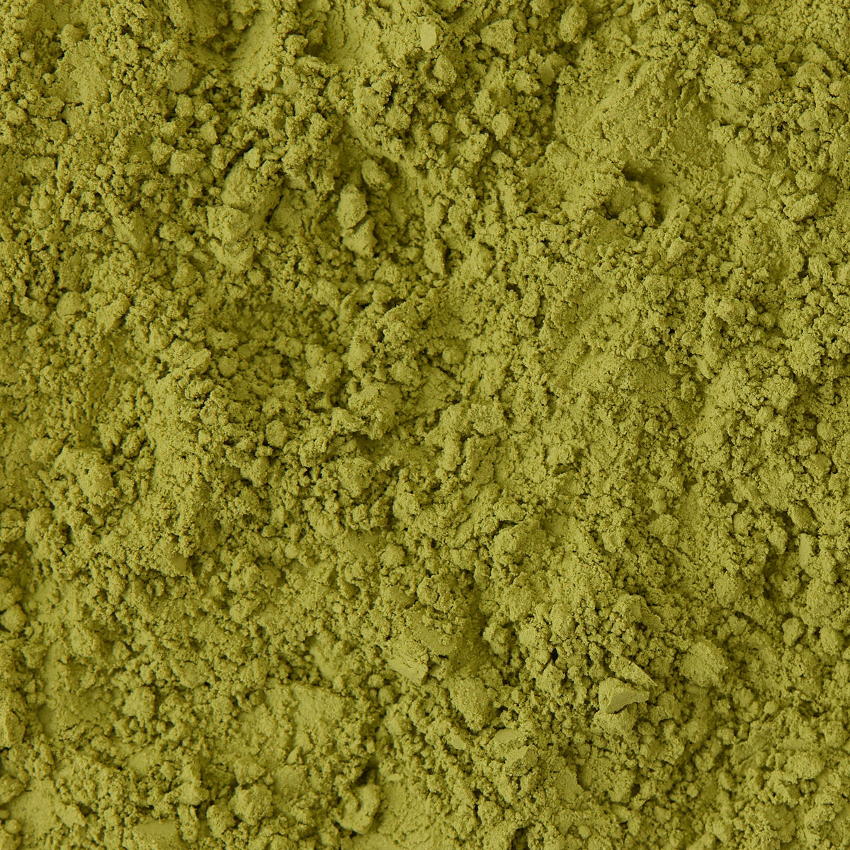 Close-up of finely ground green powder with a slightly uneven, crumbly texture, resembling matcha or green tea powder.