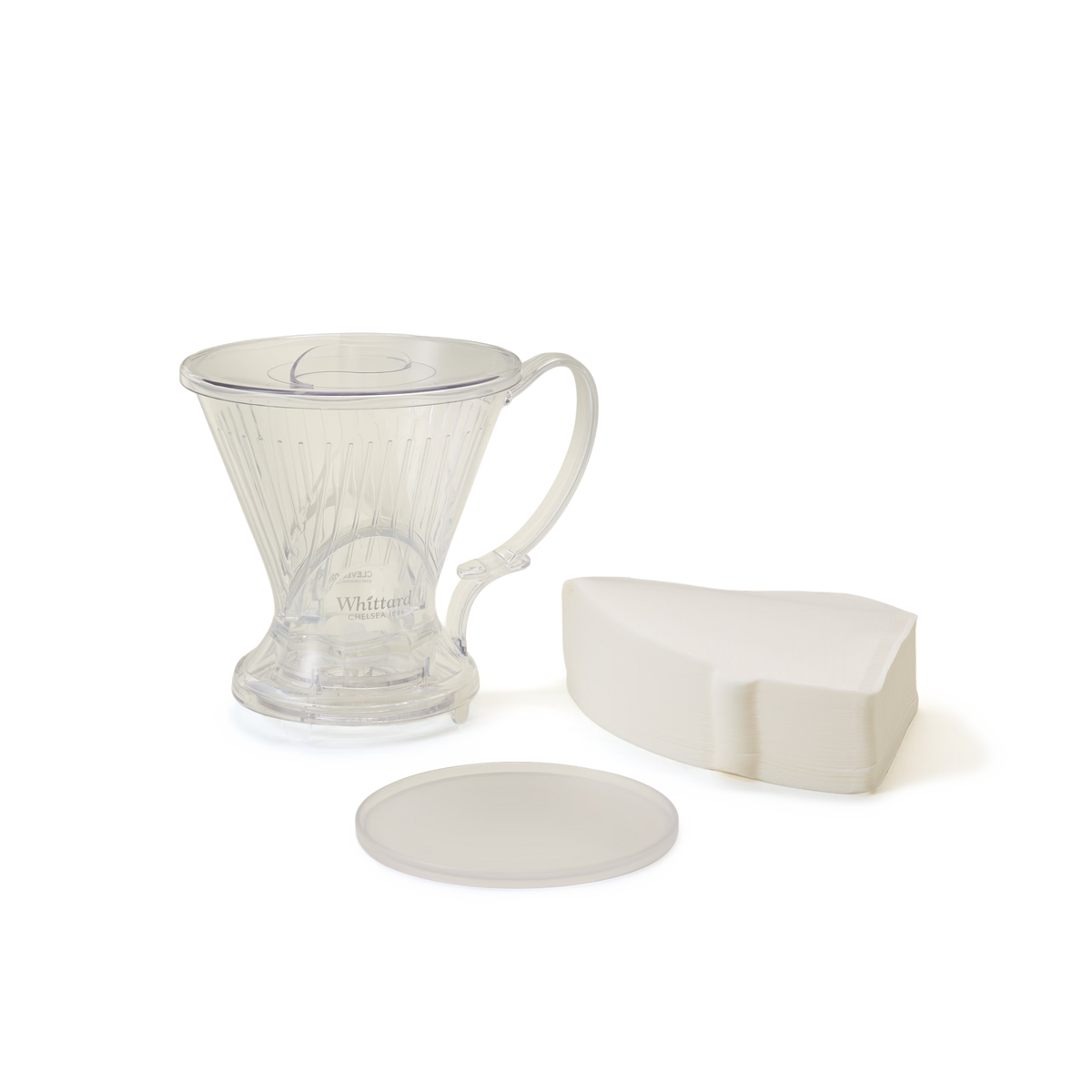 A clear plastic coffee dripper with a handle, a stack of white coffee filters, and a round lid are arranged on a plain white background.