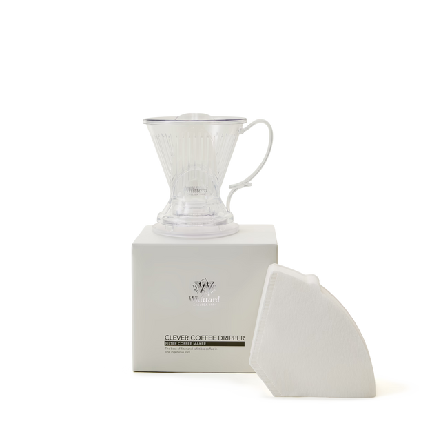 A transparent plastic coffee dripper sits on a white box labeled Clever Coffee Dripper, with a stack of white paper filters leaning against the box, all on a plain white background.