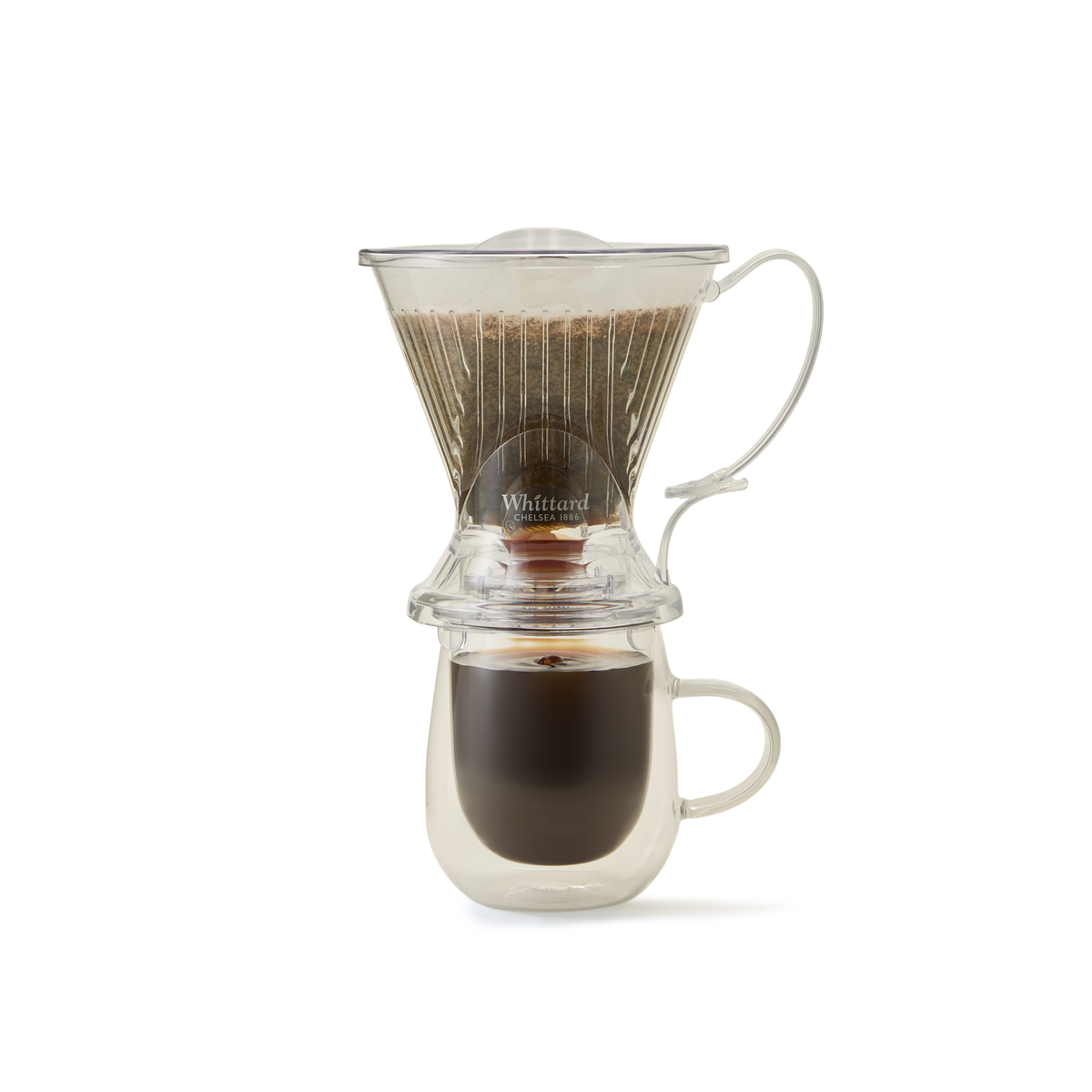 A glass pour-over coffee maker with a filter and ground coffee sits atop a glass mug, brewing fresh coffee as the liquid drips down into the cup below.