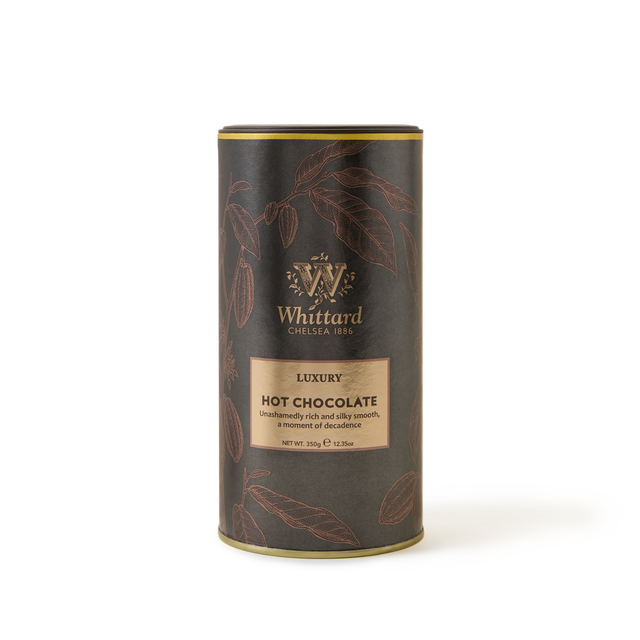 A cylindrical tin of Whittard Luxury Hot Chocolate with gold accents and illustrations of cocoa pods on a dark background. The label describes it as unashamedly rich and silky smooth..