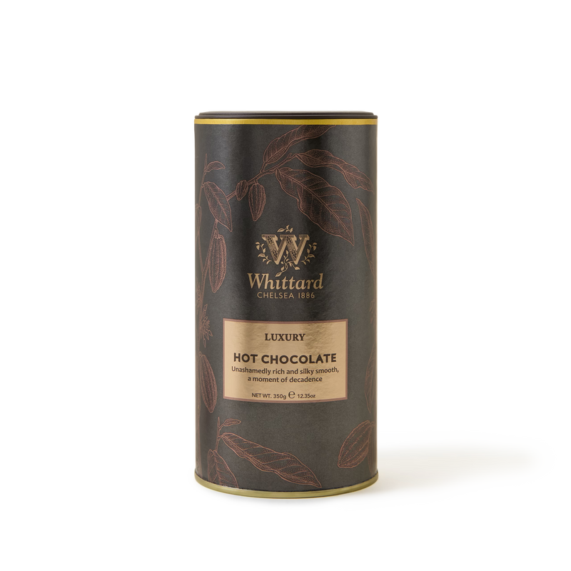 A cylindrical tin of Whittard Luxury Hot Chocolate with gold accents and illustrations of cocoa pods on a dark background. The label describes it as unashamedly rich and silky smooth..