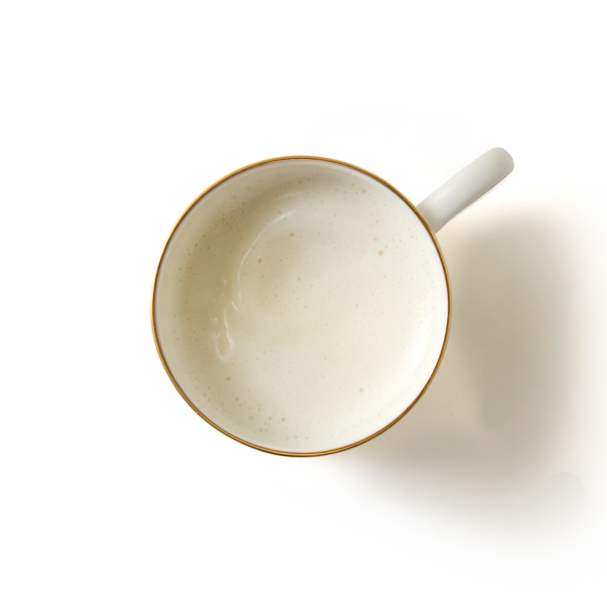 A top-down view of a white cup filled with Luxury White Hot Chocolate, its creamy froth contrasting against the white background.