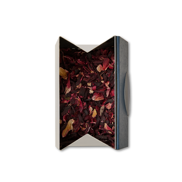 A rectangular open box of Pure Hibiscus Loose Infusion, filled with mostly dark red dried petals and a few yellow pieces, viewed from above on a white background.