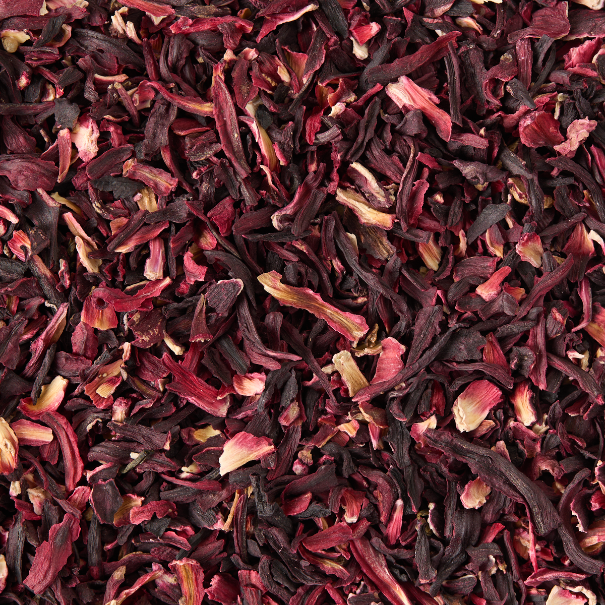 Close-up, top-down view of Pure Hibiscus Loose Infusion. The dried hibiscus petals display a deep red color, with rough and irregular textures—mixing dark crimson petals and small fragments for a dense, textured appearance.