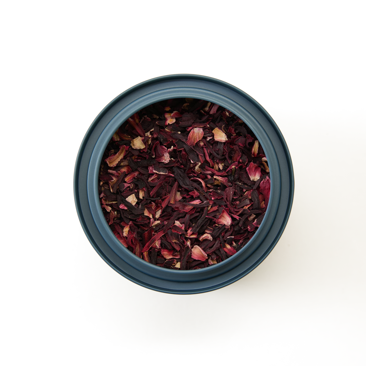 A round container filled with Pure Hibiscus Loose Infusion is viewed from above, revealing deep red and purple hibiscus petals that emphasize the product’s natural purity. Ideal for brewing hibiscus tea, this caffeine-free infusion stands out vividly against a plain white background.