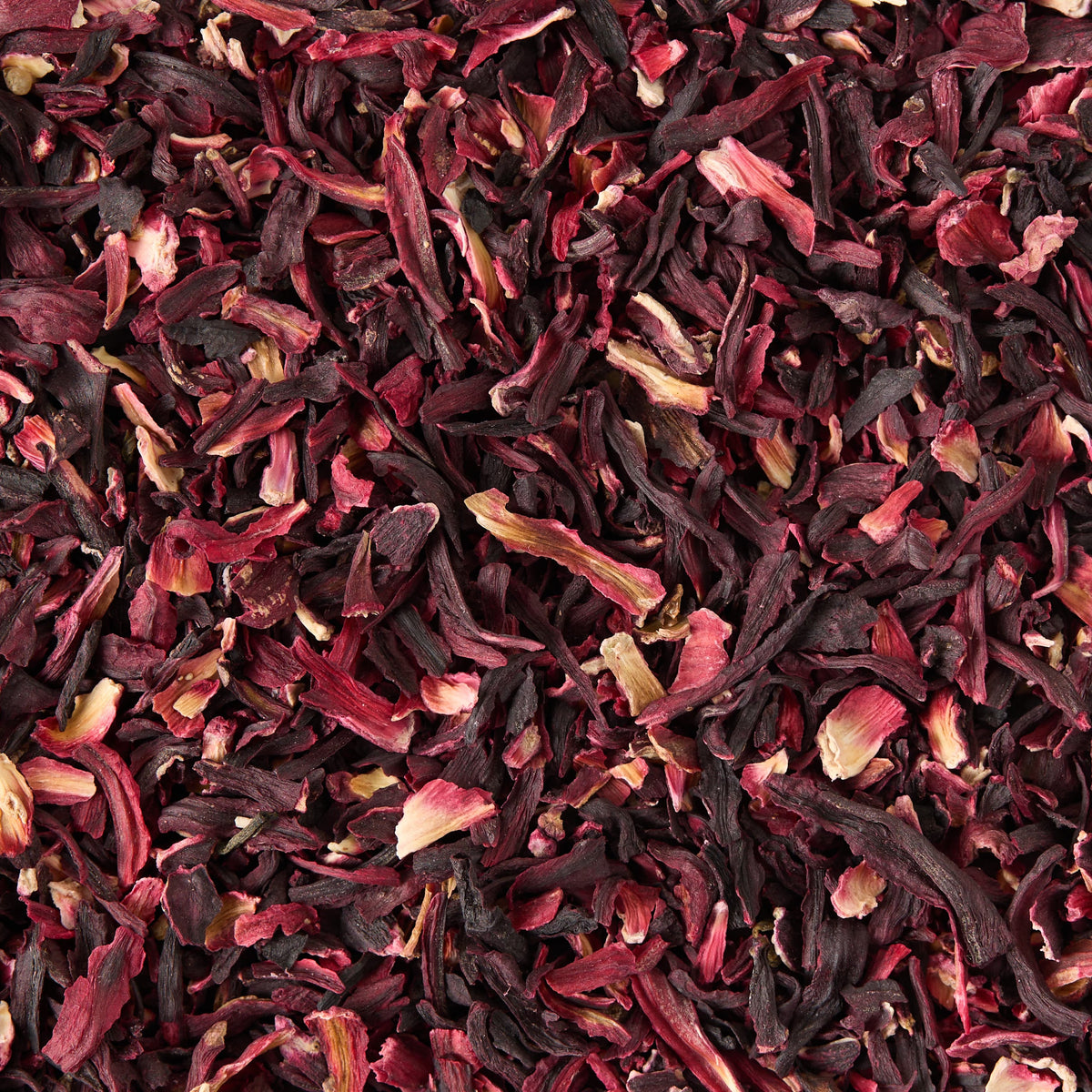 A close-up view of Pure Hibiscus Loose Infusion, featuring dried hibiscus petals in rich shades of red, purple, and pink layered together in a textured pattern—ideal for brewing a caffeine-free tea or preparing a loose hibiscus infusion.