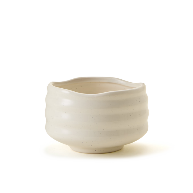 A cream-colored, wavy-rimmed ceramic bowl with a subtle horizontal ribbed texture sits on a white background.