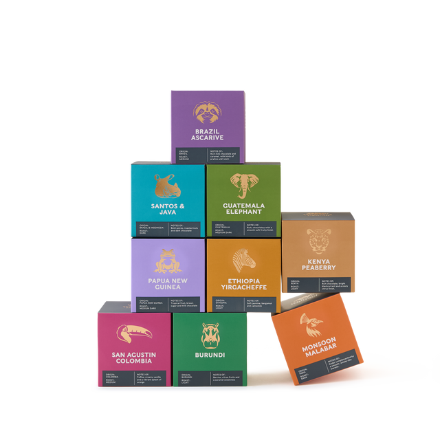 Nine colorful coffee boxes from the Coffees of the World Gift Set are stacked in a pyramid shape, each labeled with a country or region name and featuring an illustrated animal on the front—a vibrant showcase of global coffee origins. The plain white background highlights this exceptional collection.