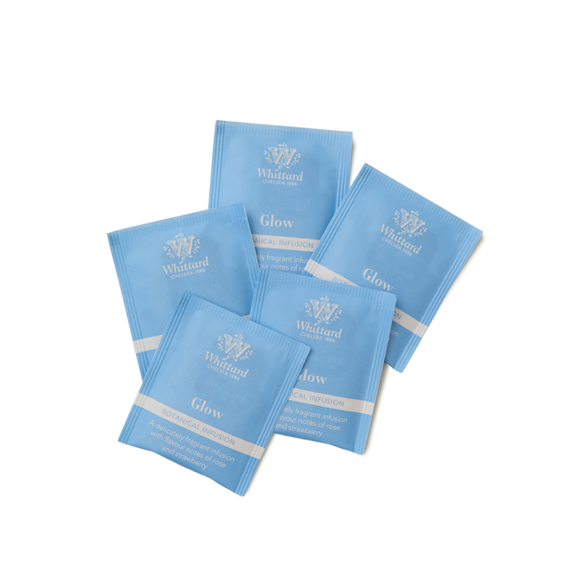 Five blue sachets of Glow Botanical Wellness Infusion Teabags are spread out on a white background. Each sachet displays the brand name and tea type in white text, highlighting the unique blend of green tea, hibiscus, and apple infusion for a naturally vibrant taste.