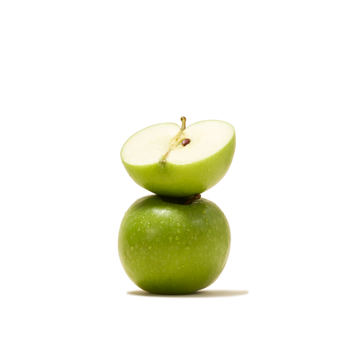 A whole green apple with a half apple balanced on top, revealing the cut side and seeds against a plain white background—an image echoing the fresh flavors captured in Turkish Apple Flavour Instant Tea, celebrated for its role in Turkish hospitality.