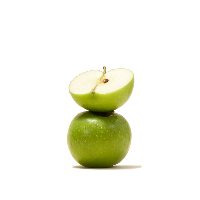 A whole green apple with a half apple balanced on top, revealing the cut side and seeds against a plain white background—an image echoing the fresh flavors captured in Turkish Apple Flavour Instant Tea, celebrated for its role in Turkish hospitality.