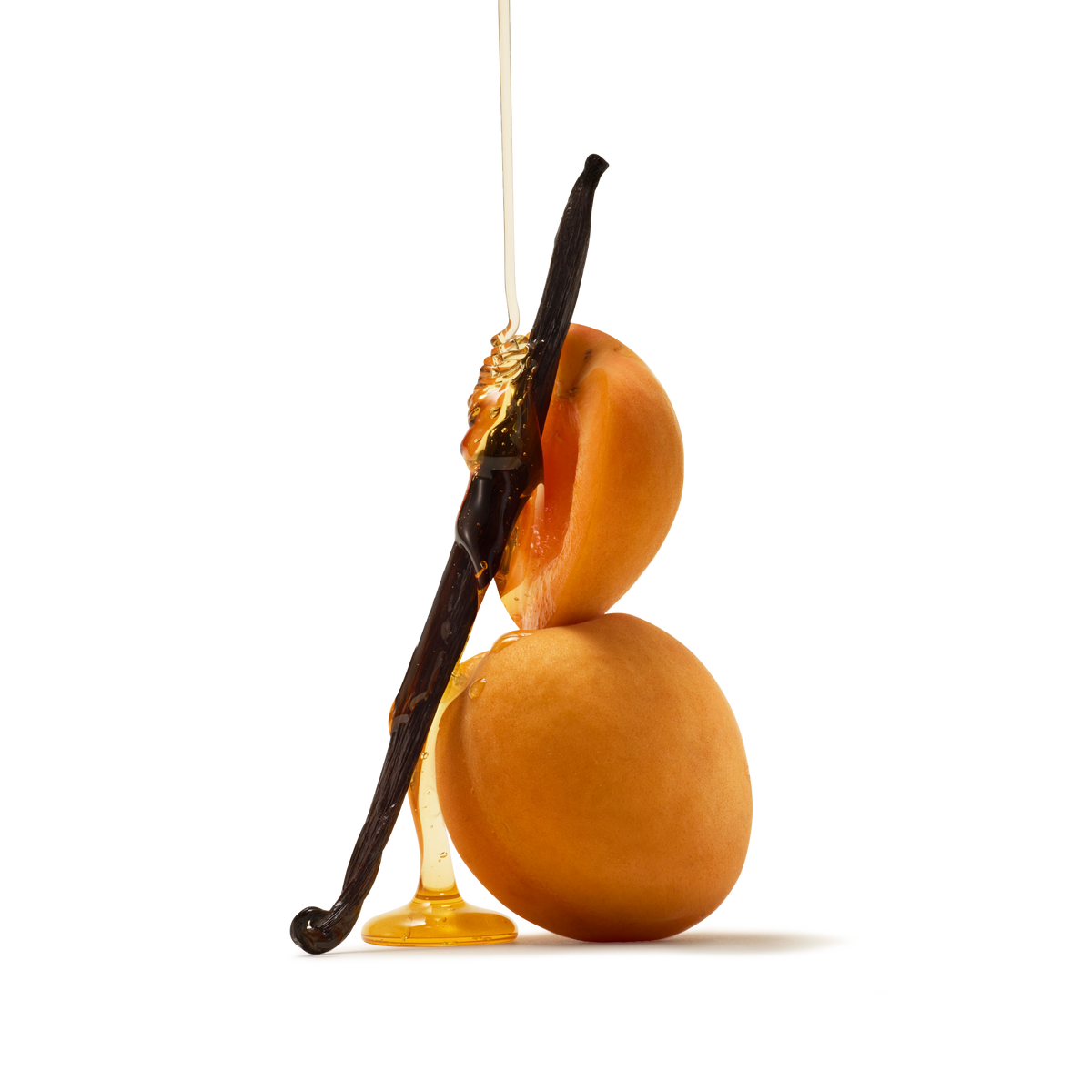 Two apricots stacked with a vanilla bean leaning against them, drizzled with honey, on a white background.