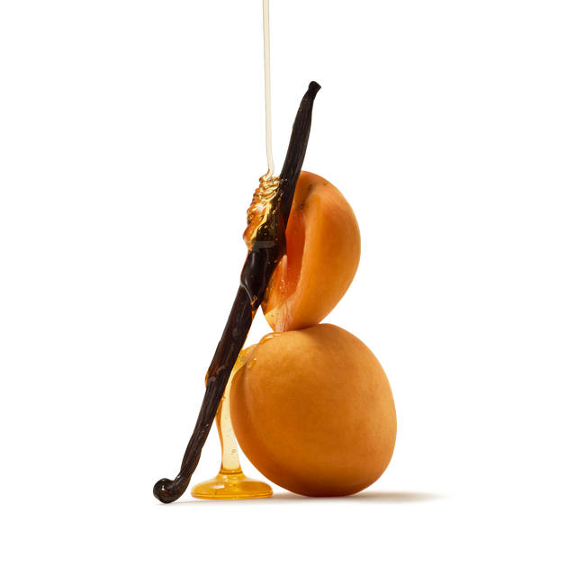 Two apricots stacked with a vanilla bean leaning against them, drizzled with honey, on a white background.