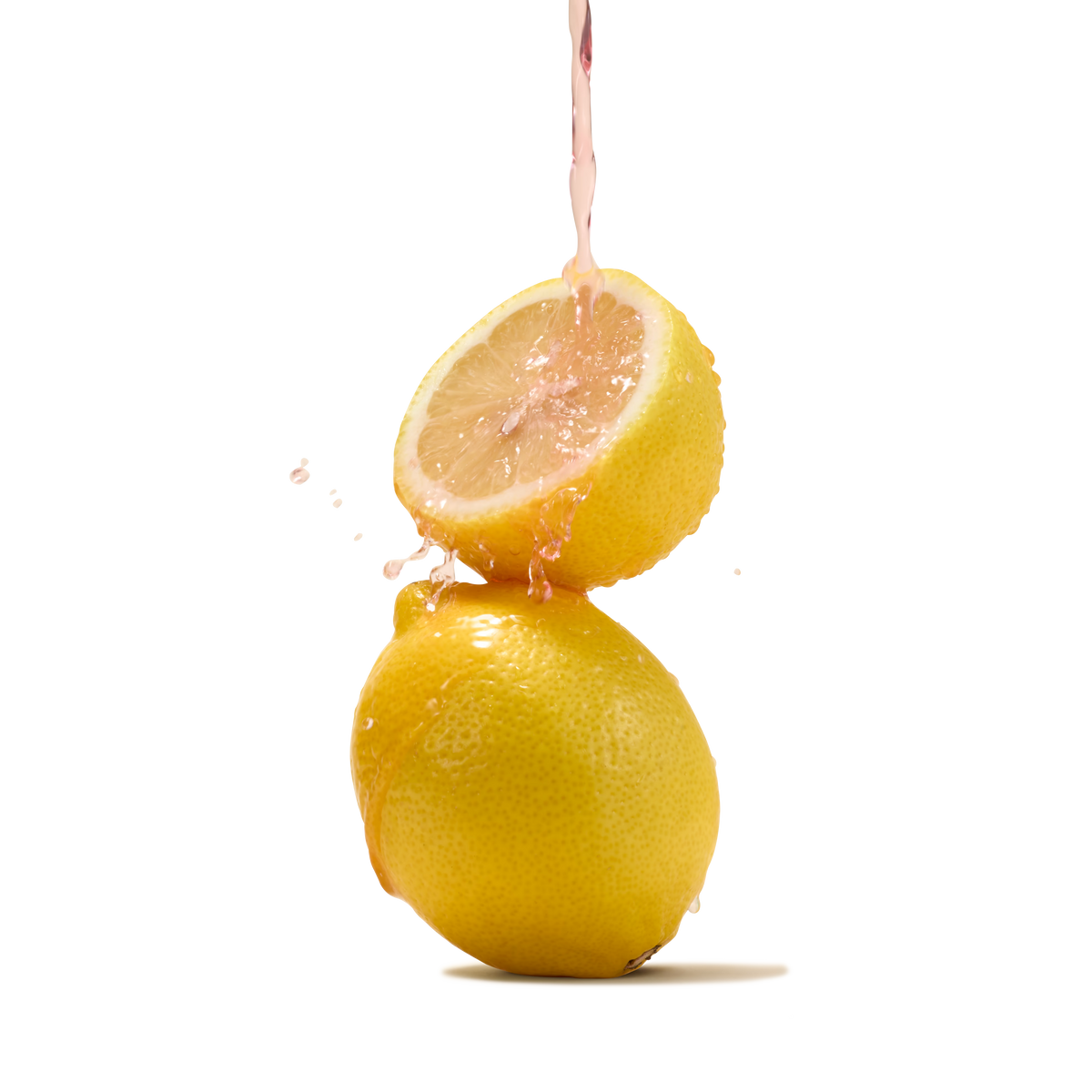 A stream of pink liquid splashes onto half a lemon balanced atop a whole lemon against a white background, capturing the lively essence of Pink Lemonade Flavour Instant Tea—a refreshing classic summer beverage.
