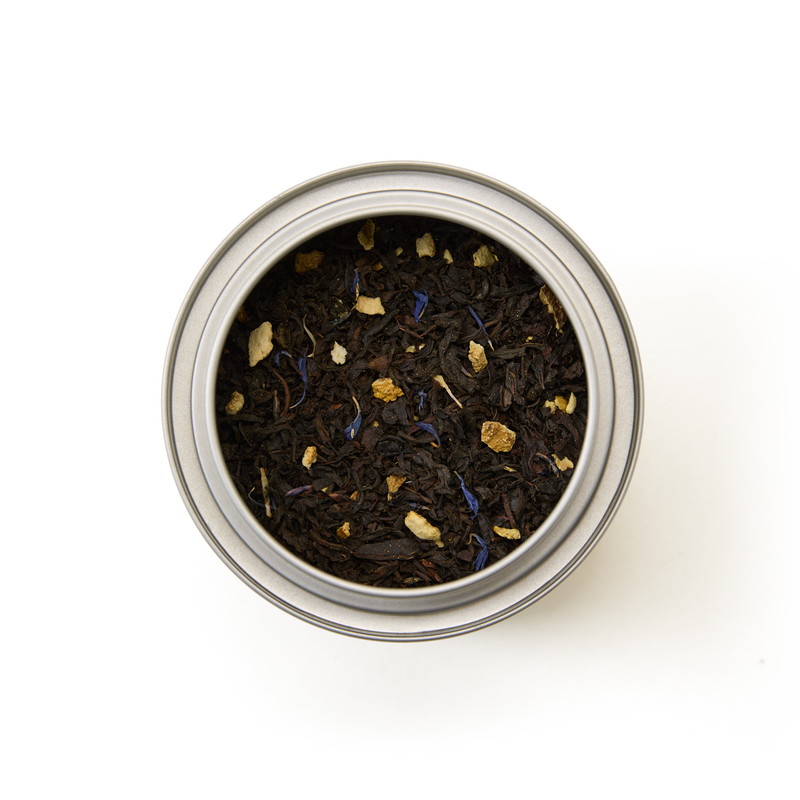 A top view of the Tea Discoveries Earl Grey Caddy—a metal tin filled with loose leaf black tea blended with small dried fruit pieces and vibrant blue cornflowers—set against a white background.
