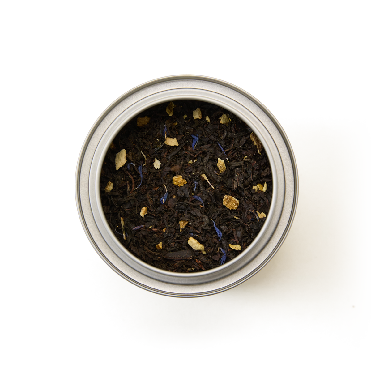 A top-down view of the Tea Discoveries Earl Grey Caddy, a round metal tin containing loose leaf Earl Grey tea made with dark Ceylon black tea leaves, delicate blue flower petals, subtle hints of bergamot, and small pieces of dried fruit or spice, set against a white background.