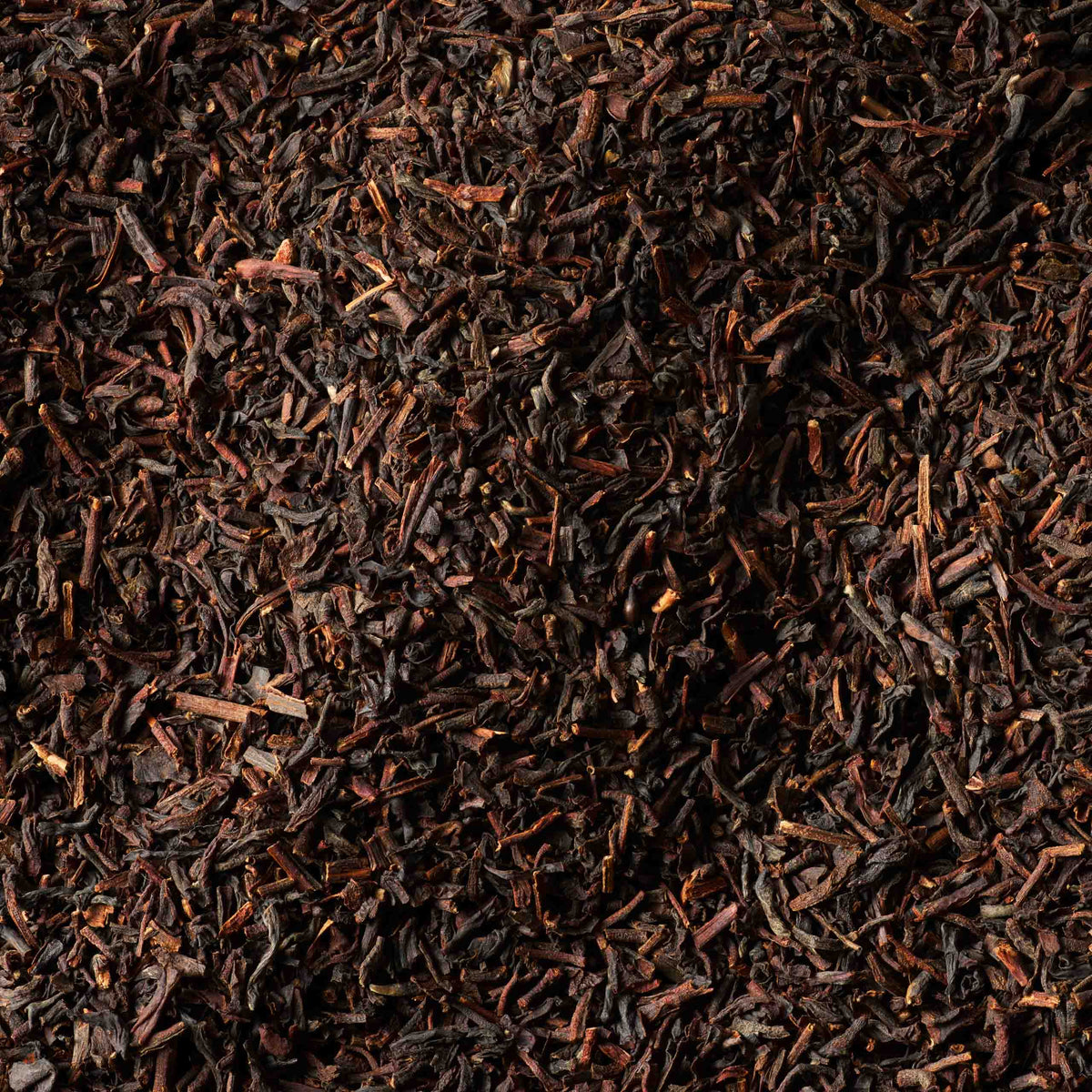 Loose, dried black tea leaves from the Tea Discoveries English Breakfast Tea Caddy are scattered densely, creating a textured surface in deep brown and black hues with subtle reddish-brown tones.