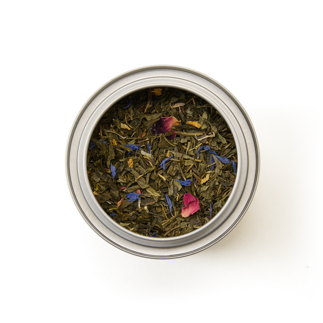 A round metal Tea Discoveries Mango & Bergamot Tea Caddy filled with loose leaf tea, viewed from above on a white background.