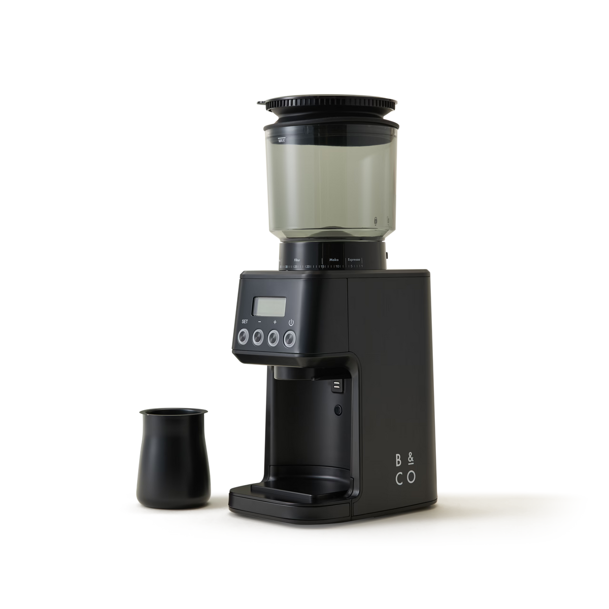 A black electric coffee grinder with a digital display and buttons sits next to a small black carafe on a white background. The grinder has a transparent bean hopper on top and B & CO printed on its side.