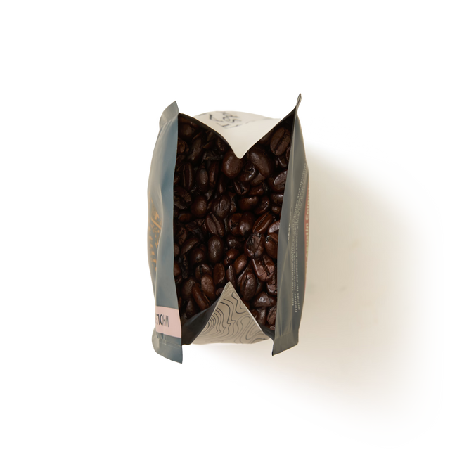 An open bag of Monsoon Malabar Coffee Beans Valve Pack viewed from above, with the dark roasted beans visible inside and the bag edges folded outward against a white background.